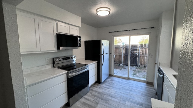 kitchen featuring white cabinetry, light stone counters, stainless steel appliances, a textured ceiling, and light hardwood / wood-style flooring