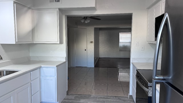 kitchen with stainless steel fridge, light stone counters, white cabinets, ceiling fan, and sink