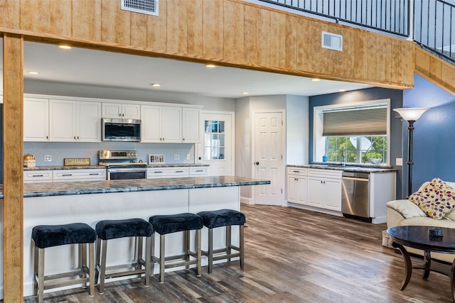 kitchen with dark stone counters, appliances with stainless steel finishes, dark wood-type flooring, and white cabinets