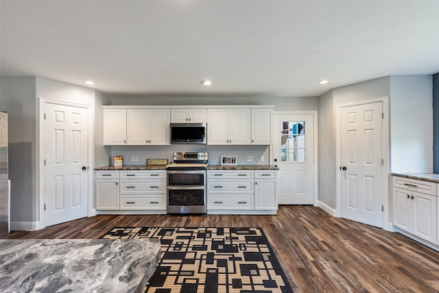 kitchen featuring appliances with stainless steel finishes, dark wood-type flooring, white cabinets, and dark stone counters