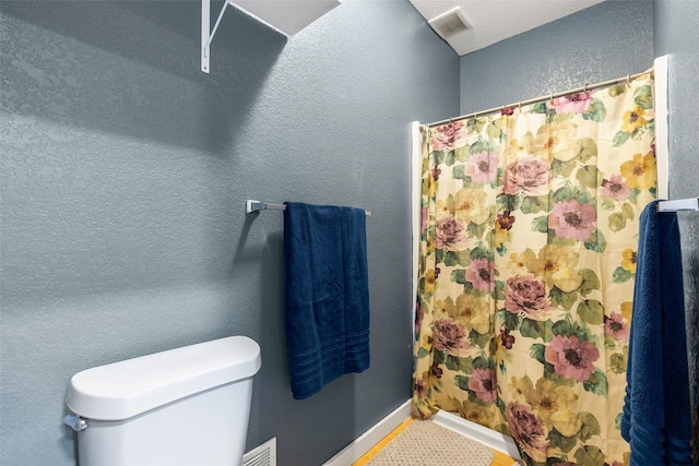 bathroom with visible vents, baseboards, toilet, a shower with curtain, and a textured wall