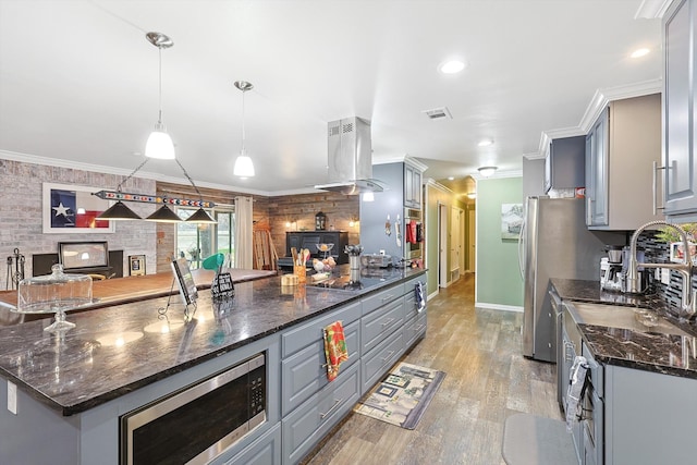 kitchen with stainless steel appliances, light wood-type flooring, gray cabinetry, wall chimney range hood, and dark stone countertops