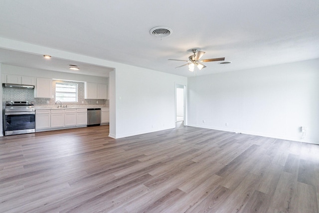 unfurnished living room featuring light wood finished floors, visible vents, baseboards, ceiling fan, and a sink