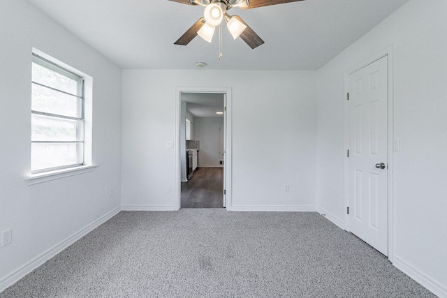 empty room featuring ceiling fan, dark carpet, and baseboards