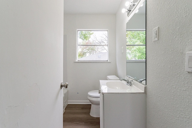 bathroom with a textured wall, toilet, vanity, wood finished floors, and baseboards