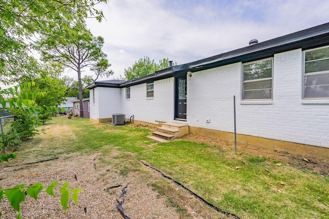 back of house with central air condition unit, a lawn, and brick siding