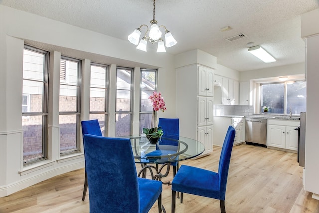 dining area with a textured ceiling, light hardwood / wood-style flooring, a notable chandelier, and sink