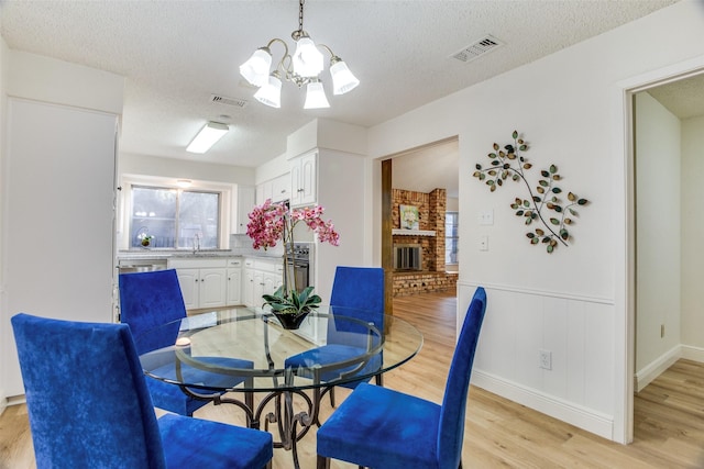 dining area with sink, light hardwood / wood-style floors, a textured ceiling, and an inviting chandelier