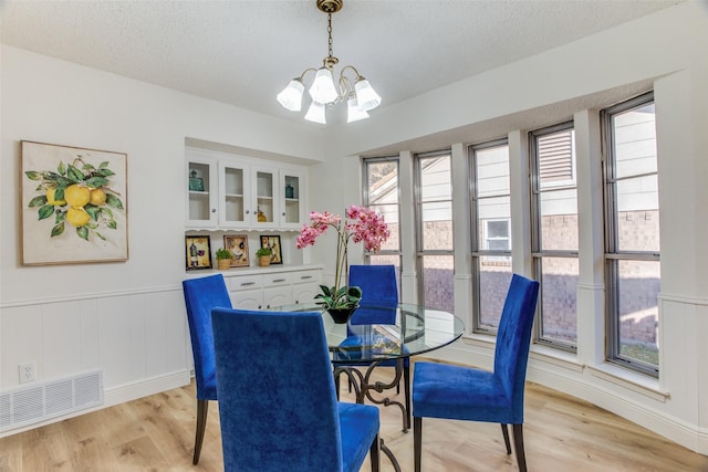 dining room featuring a wealth of natural light, light hardwood / wood-style flooring, a textured ceiling, and a notable chandelier