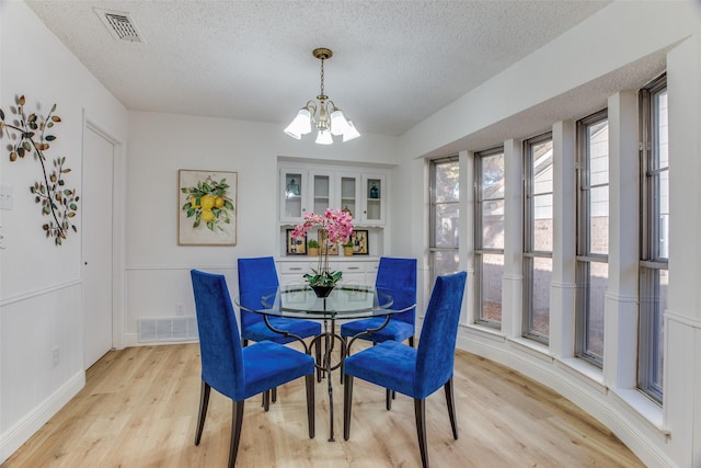 dining space featuring light hardwood / wood-style flooring, a chandelier, and a textured ceiling