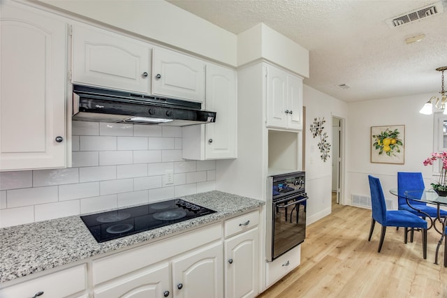 kitchen with hanging light fixtures, white cabinets, black appliances, and light hardwood / wood-style floors