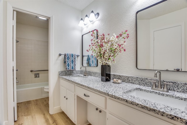 full bathroom featuring vanity, tiled shower / bath combo, toilet, a textured ceiling, and wood-type flooring