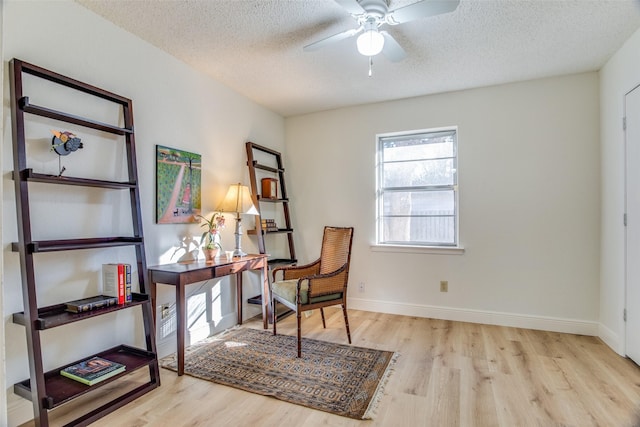 sitting room with ceiling fan, light wood-type flooring, and a textured ceiling