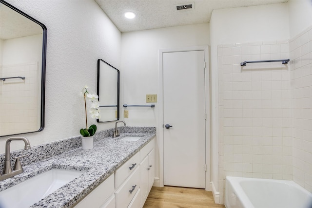 bathroom with hardwood / wood-style flooring, vanity, a textured ceiling, and tiled shower / bath