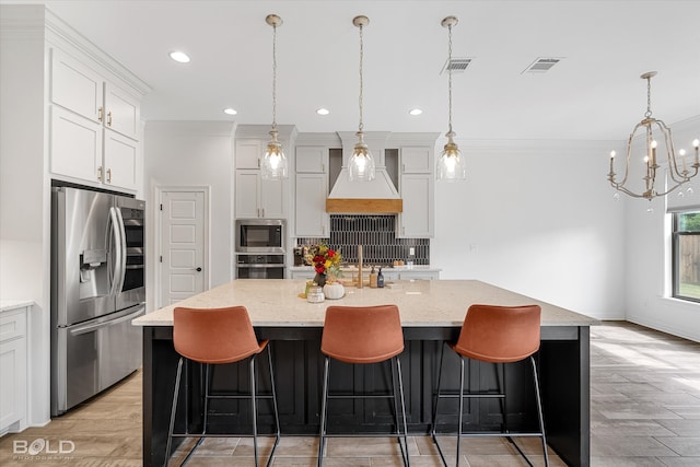 kitchen with pendant lighting, custom exhaust hood, light stone counters, appliances with stainless steel finishes, and a center island with sink