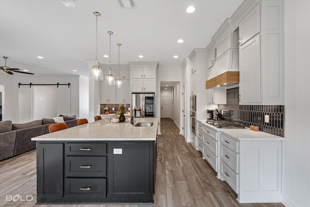 kitchen with a kitchen island with sink, a barn door, hanging light fixtures, white cabinets, and light hardwood / wood-style floors