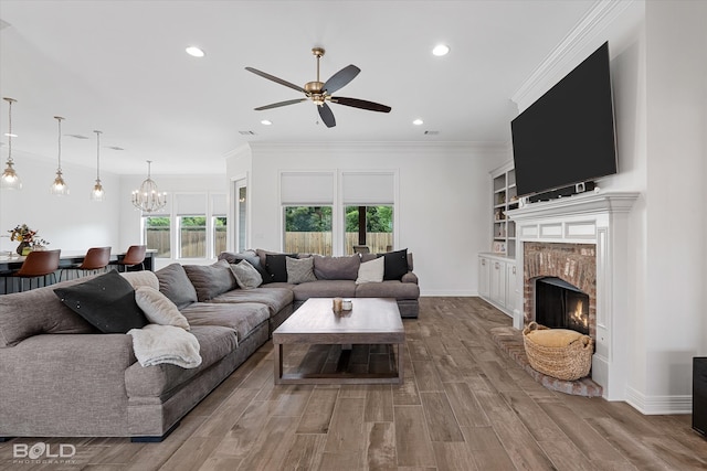 living room featuring ceiling fan with notable chandelier, wood-type flooring, a wealth of natural light, and a brick fireplace