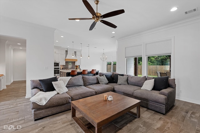 living room with ceiling fan with notable chandelier, light wood-type flooring, and crown molding