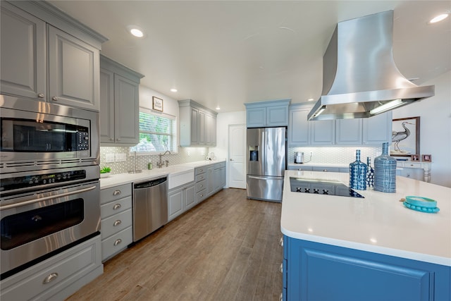 kitchen featuring island exhaust hood, stainless steel appliances, sink, decorative backsplash, and hardwood / wood-style flooring