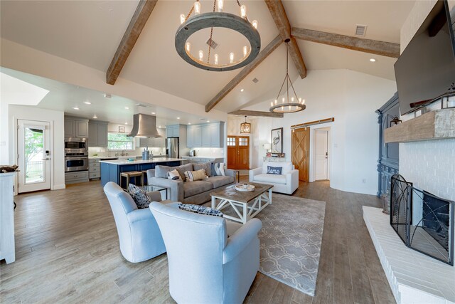 living room with light wood-type flooring, a fireplace, a chandelier, and beam ceiling