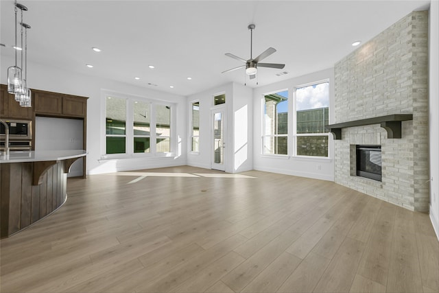 unfurnished living room with ceiling fan, a stone fireplace, and light hardwood / wood-style flooring