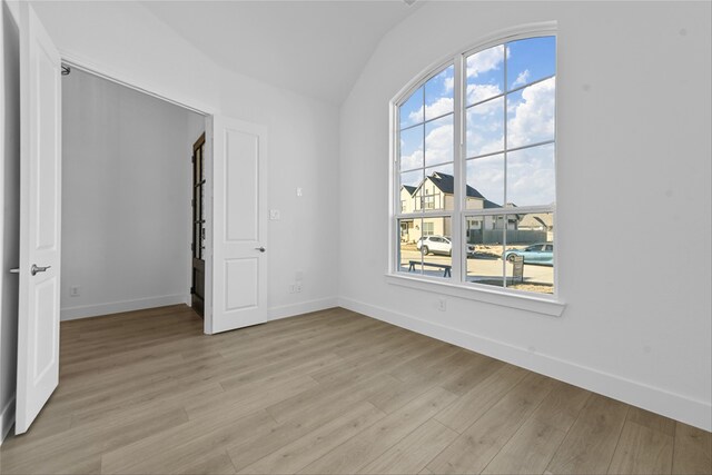 empty room with light wood-type flooring and vaulted ceiling