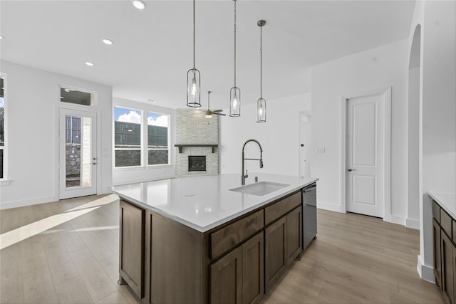 kitchen with dishwasher, light hardwood / wood-style flooring, decorative light fixtures, sink, and a center island with sink