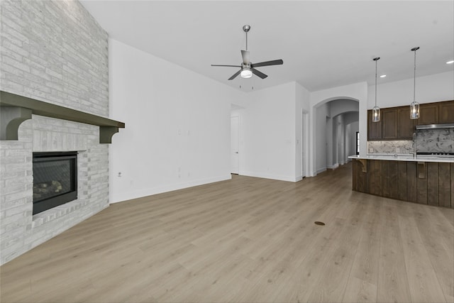 unfurnished living room with ceiling fan, a stone fireplace, and light hardwood / wood-style floors