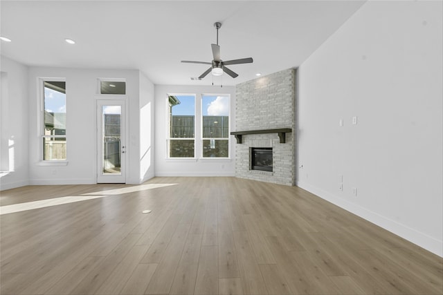 unfurnished living room featuring ceiling fan, light hardwood / wood-style flooring, and a stone fireplace