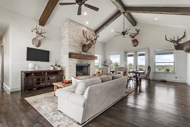 living room featuring ceiling fan, a wealth of natural light, a stone fireplace, and dark wood-type flooring