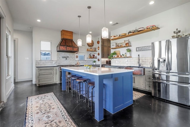 kitchen featuring backsplash, premium range hood, pendant lighting, stainless steel fridge with ice dispenser, and a center island