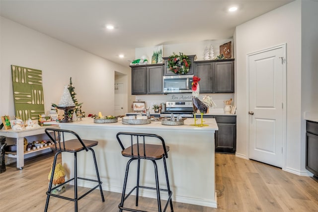 kitchen featuring a breakfast bar, stainless steel appliances, light hardwood / wood-style flooring, and an island with sink