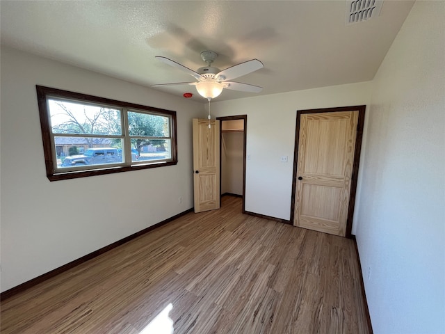 unfurnished bedroom featuring hardwood / wood-style flooring, a closet, a walk in closet, and ceiling fan