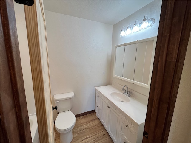 bathroom with a bath, vanity, hardwood / wood-style floors, and toilet