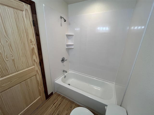 bathroom with washtub / shower combination, wood-type flooring, and toilet