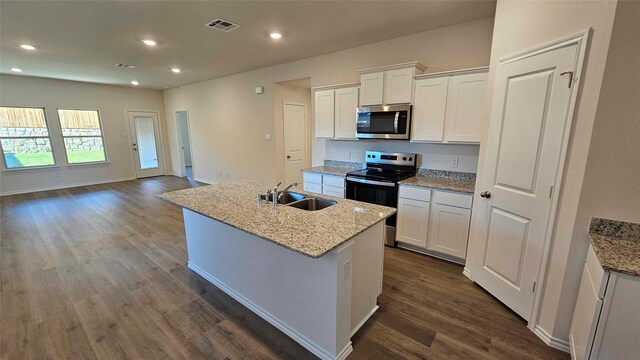 kitchen featuring light stone countertops, stainless steel appliances, a kitchen island with sink, sink, and white cabinets