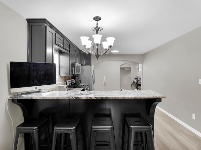 kitchen with a kitchen breakfast bar, kitchen peninsula, stainless steel appliances, light hardwood / wood-style flooring, and a notable chandelier