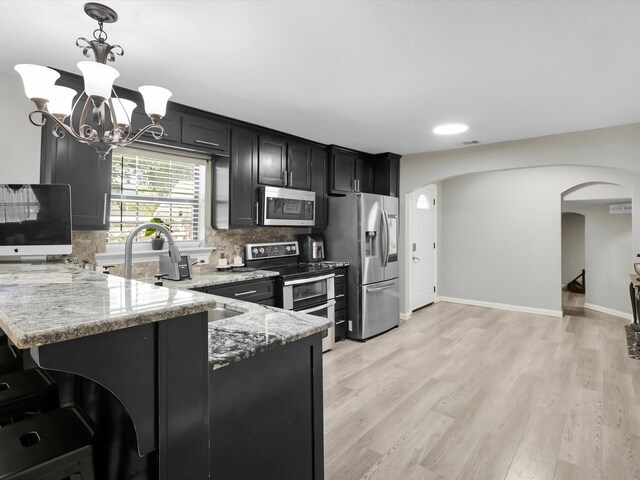 kitchen with kitchen peninsula, light stone countertops, stainless steel appliances, light wood-type flooring, and decorative light fixtures