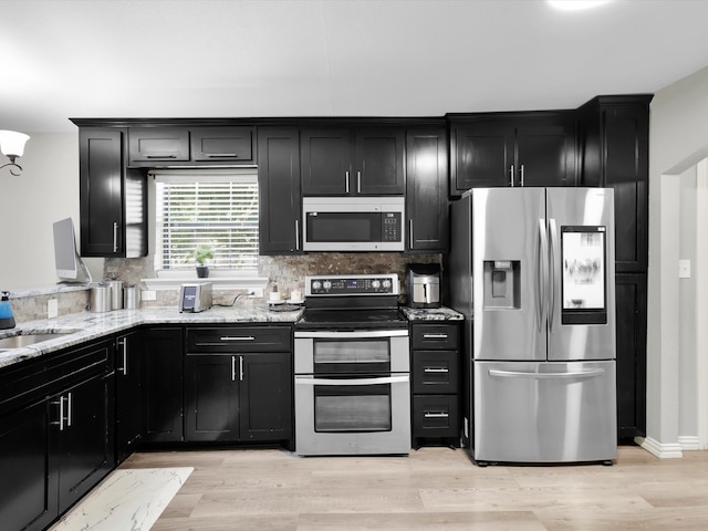 kitchen with light stone counters, sink, backsplash, stainless steel appliances, and light hardwood / wood-style floors