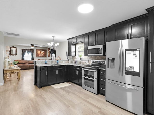 kitchen featuring pendant lighting, sink, appliances with stainless steel finishes, ceiling fan with notable chandelier, and light hardwood / wood-style floors