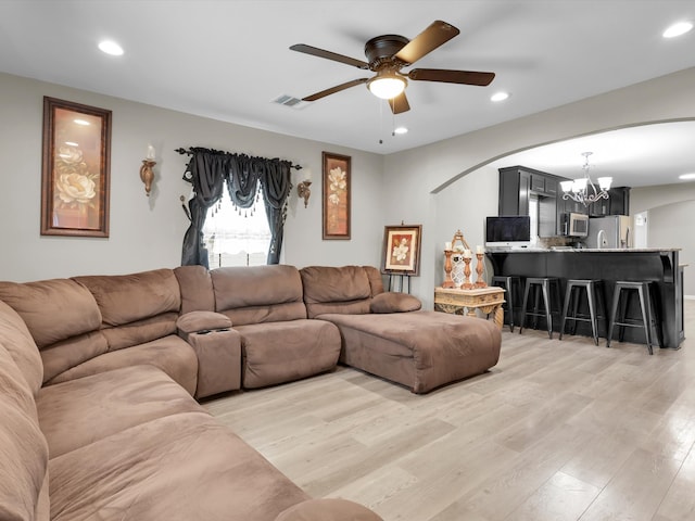 living room featuring ceiling fan with notable chandelier and light wood-type flooring