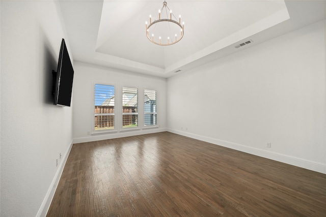 empty room with a tray ceiling, a chandelier, and dark hardwood / wood-style floors