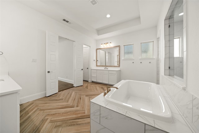 bathroom featuring a tray ceiling, vanity, a relaxing tiled tub, and parquet flooring