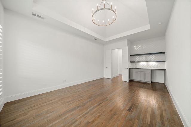 unfurnished living room with dark hardwood / wood-style flooring, a tray ceiling, and a chandelier