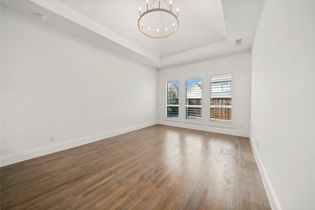 unfurnished room featuring a raised ceiling, hardwood / wood-style floors, and a chandelier