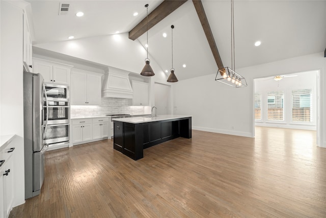 kitchen featuring premium range hood, stainless steel appliances, ceiling fan, a center island with sink, and beamed ceiling