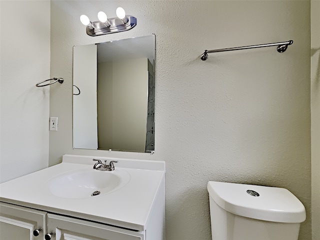 bathroom with a textured wall, toilet, and vanity