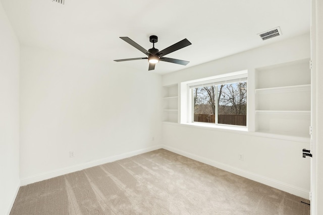 spare room with built in shelves, light colored carpet, and ceiling fan