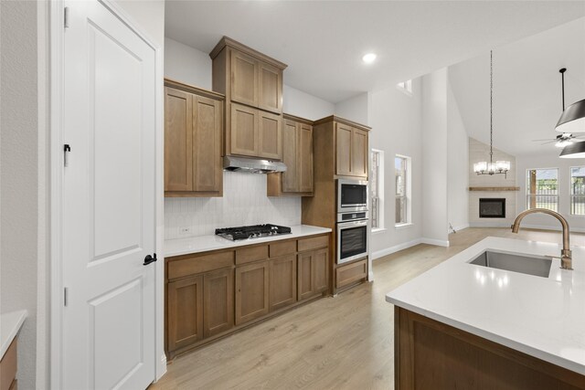 kitchen with a sink, under cabinet range hood, open floor plan, a glass covered fireplace, and stainless steel appliances