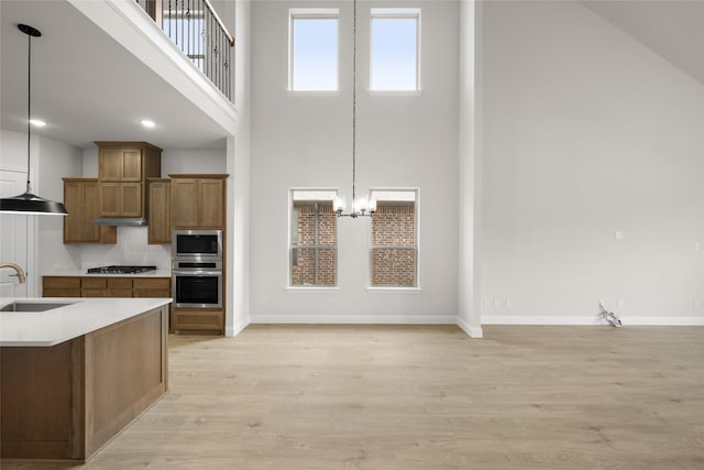 kitchen featuring light wood finished floors, decorative light fixtures, brown cabinetry, stainless steel appliances, and a sink